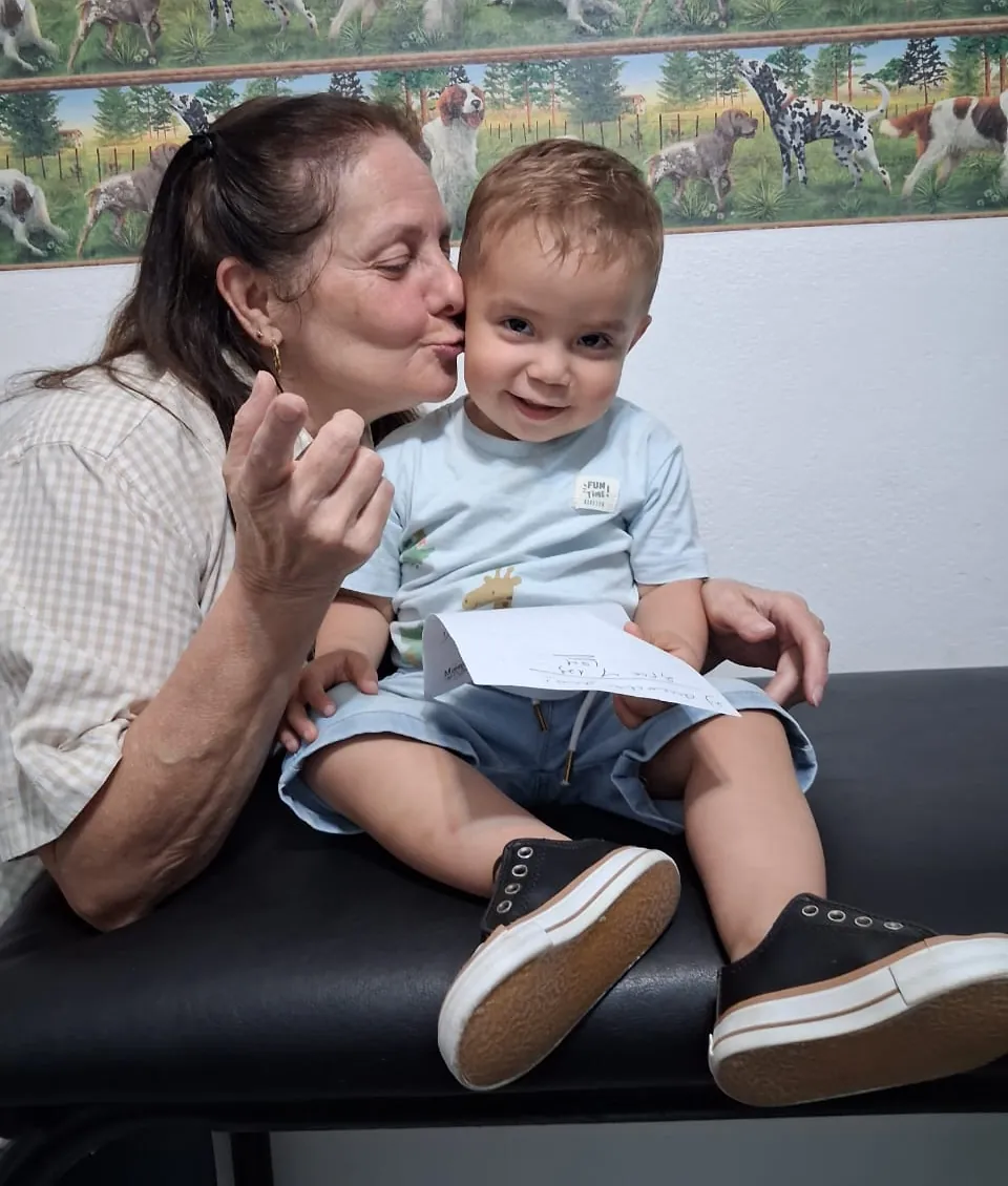 La doctora le da un beso en la mejilla a un nene que sonríe con una hoja en la mano.