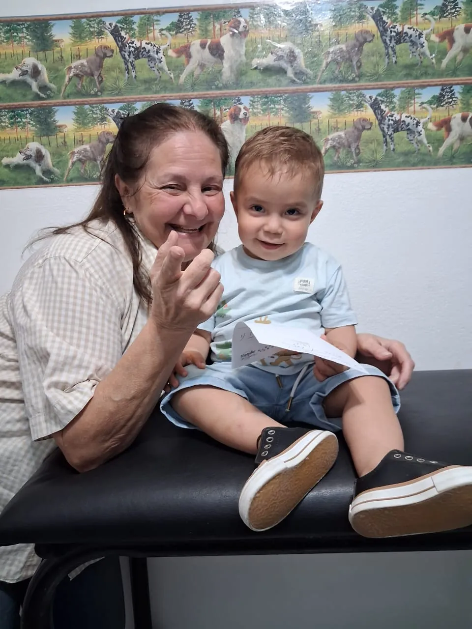 La doctora y un nene sonríen a la cámara sentados en la camilla.