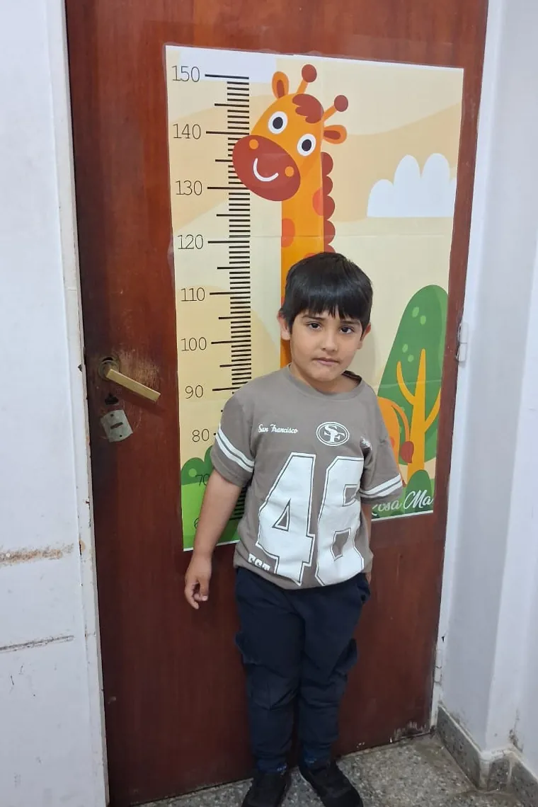 Un nene parado junto al medidor de altura con una jirafa dibujada, pegado en la puerta del consultorio.